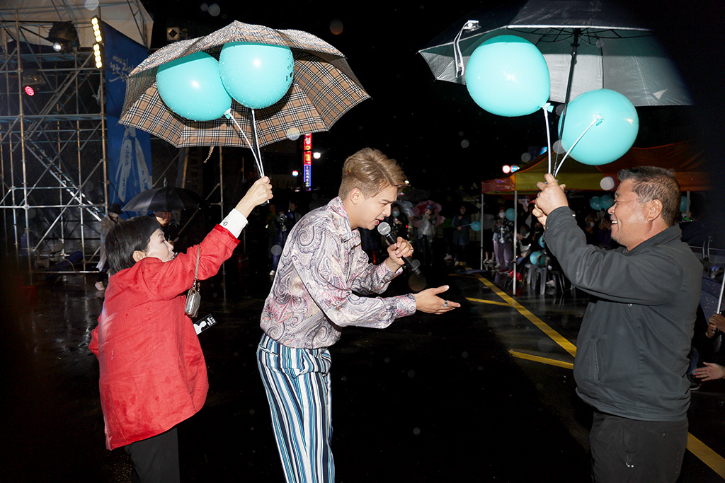 미스터 트롯 출신 류지광 씨가 객석까지 내려와 열창하자 팬클럽 회원이 우산을 씌워주고 있다.